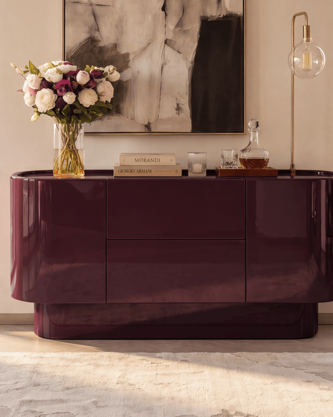 Close-up of the Velar Buffet in deep oxblood high-gloss lacquer styled with a fresh rose floral arrangement, crystal decanter tray, and candlelight.