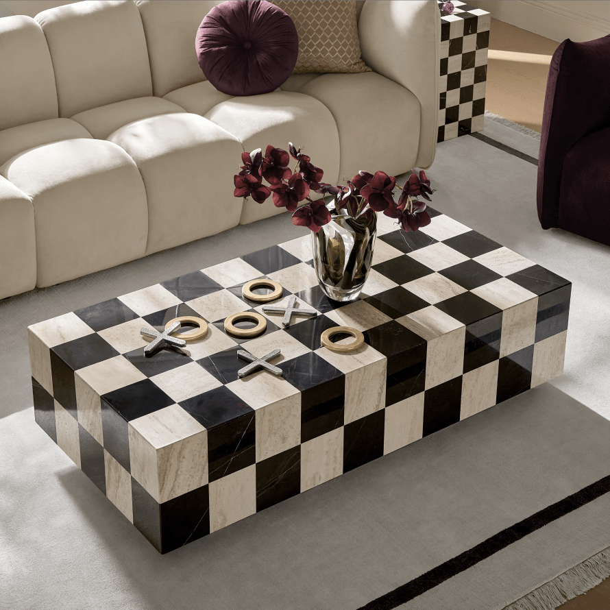 Modern black and white checkered marble block coffee table styled with brass tic-tac-toe game in front of a tufted cream sofa.