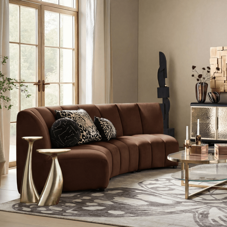 Modern brown channel-tufted curved sectional sofa with patterned throw pillows and sculptural brass side tables