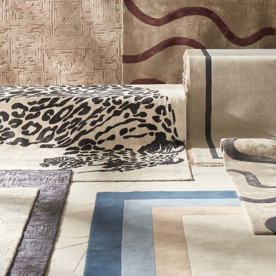 Layered display of designer area rugs featuring leopard print, geometric, and blue bordered patterns.