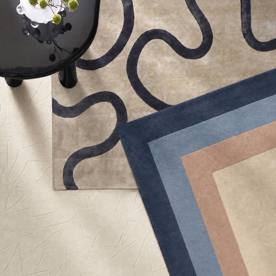 Modern overlapping area rugs showcasing deep blue wavy patterns and bordered geometric bands in rich navy and warm camel tones.