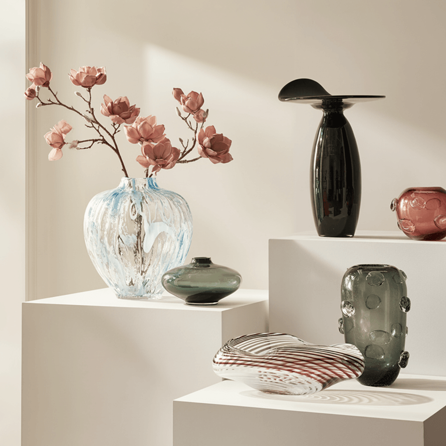 Gallery display of designer glass and ceramic vases, including a blue swirl vase with pink floral branches and modern sculptural vessels.