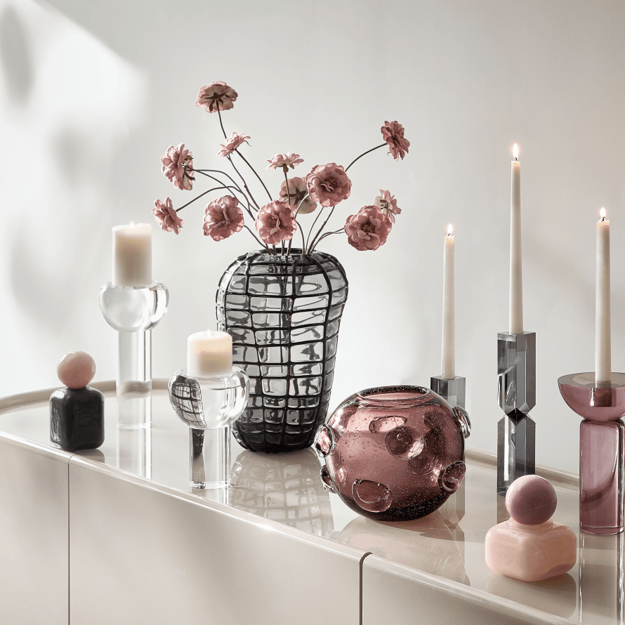Elegant console table styled with art glass vases, floral arrangement, and colorful sculptural candleholders.