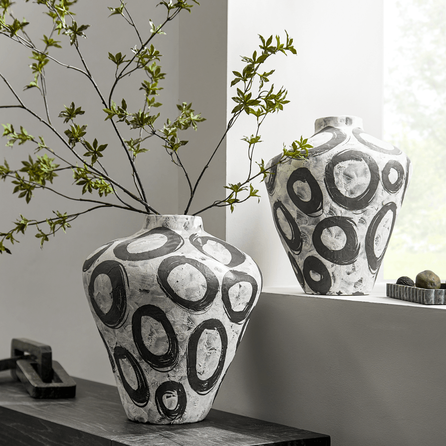 Two textured white ceramic vases with abstract black circle patterns holding green branches