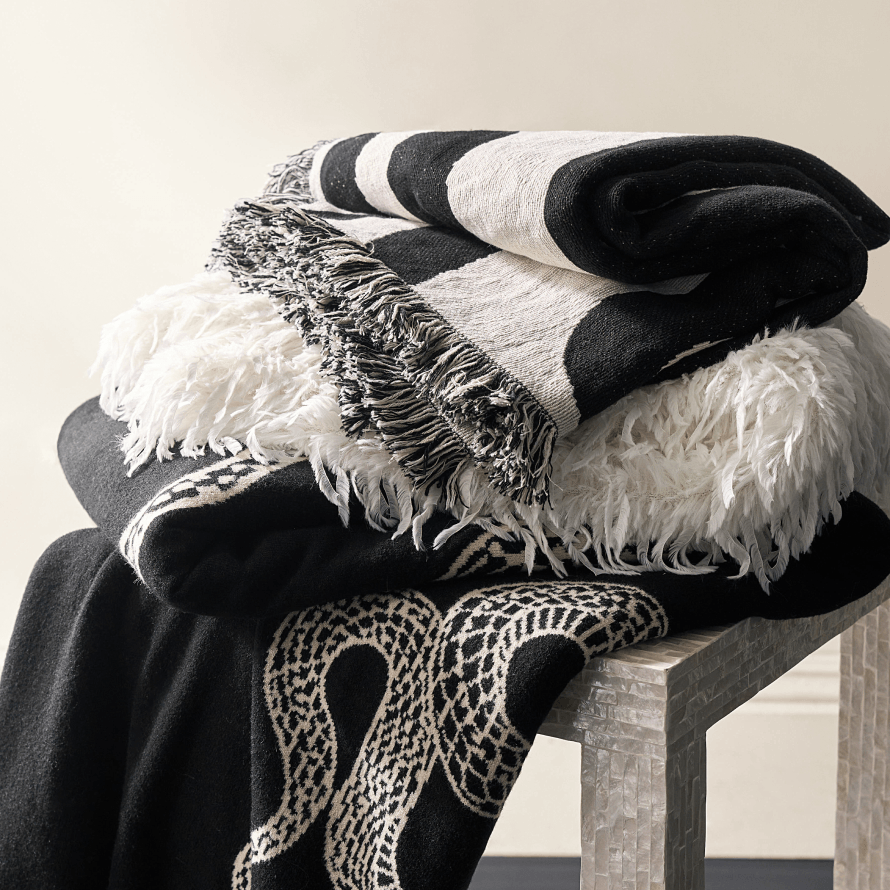 Stack of luxury black and white textiles including a snake pattern throw blanket, a striped fringe blanket, and a white faux fur throw