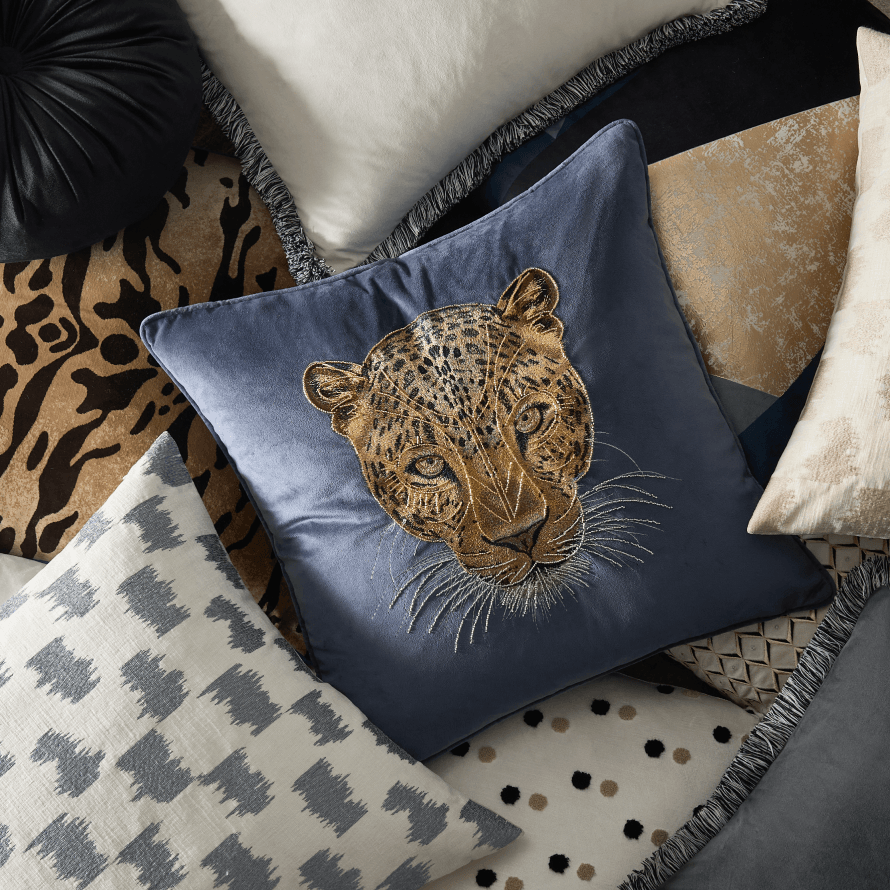 Array of luxury throw pillows showcasing an embroidered leopard velvet cushion, tiger print accents, and patterned neutral pillows.