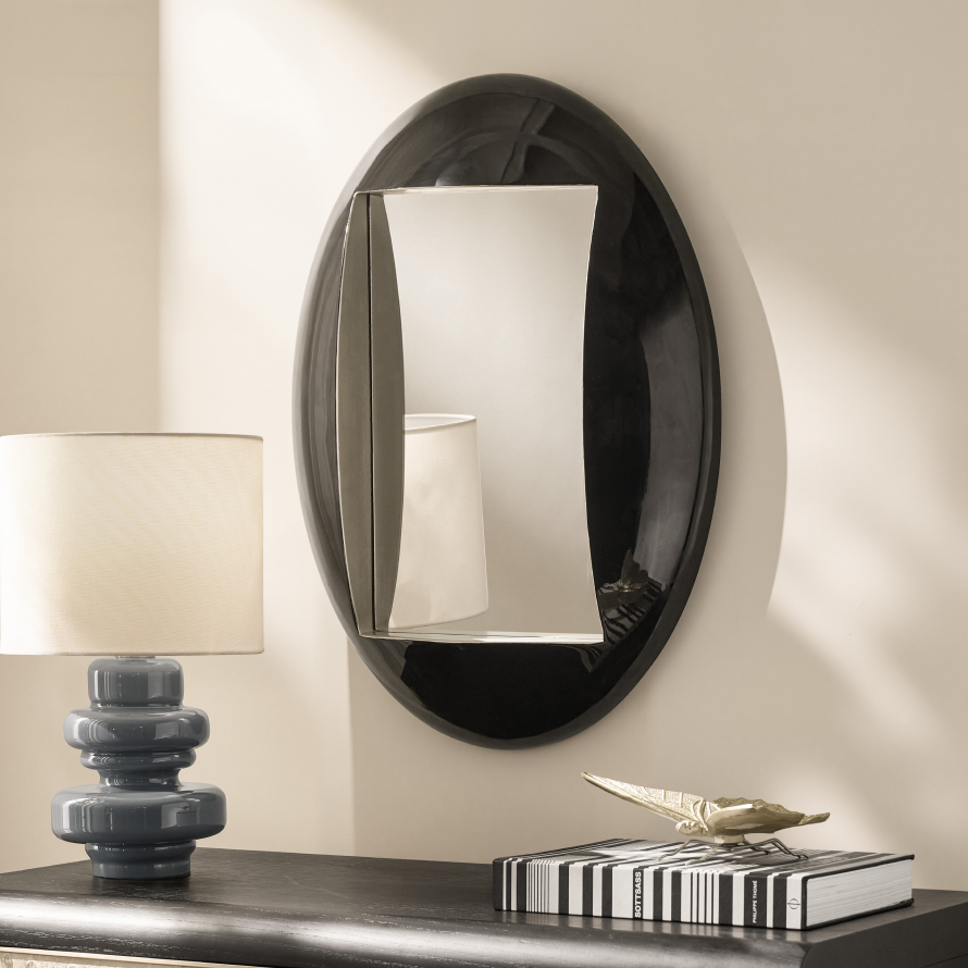 Large modern oval black wall mirror hung above a dark console table with a blue ceramic table lamp