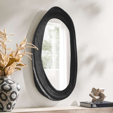 Large asymmetrical oval wall mirror with a textured black frame mounted above a console table with decorative accents