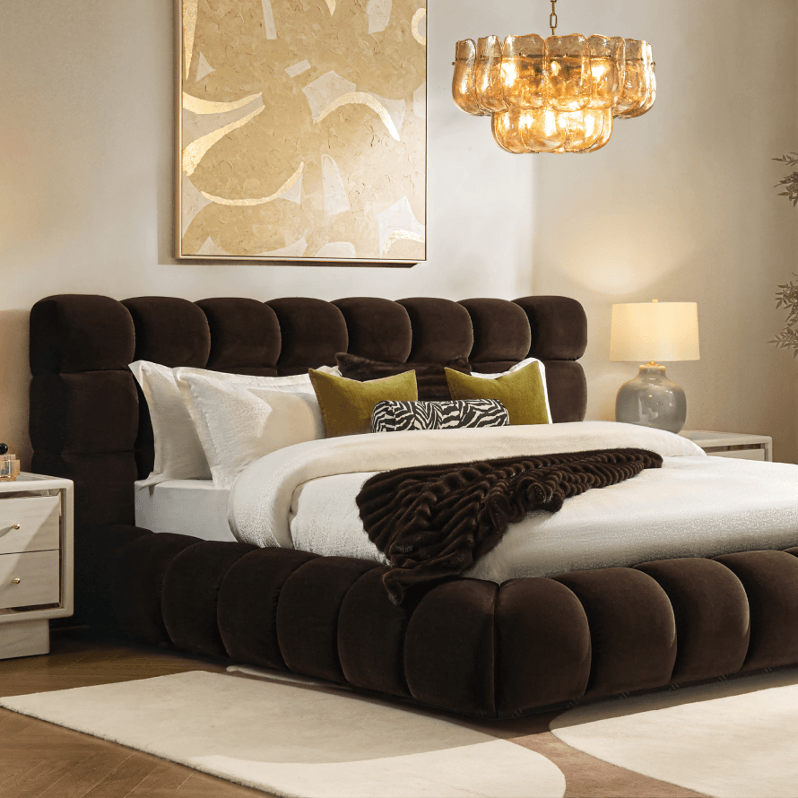 Dark velvet upholstered bed with white bedding and brown accent pillows, paired with a brown chandelier.