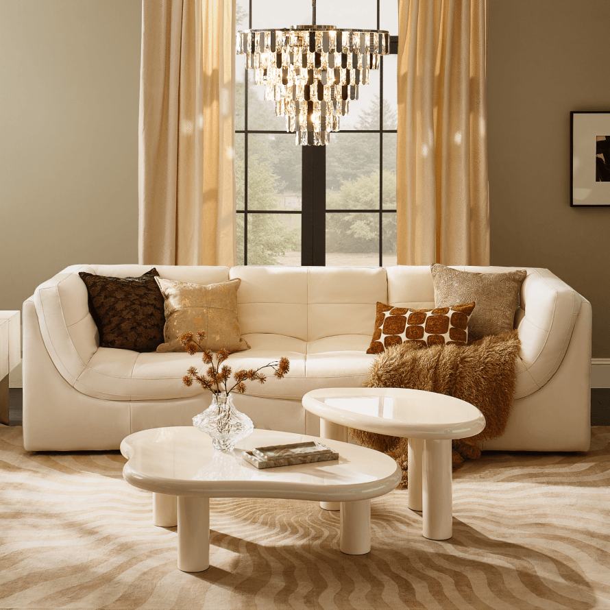 Cream modern sectional sofa with decorative pillows, low organic coffee tables, and a tiered crystal chandelier in a warm living room