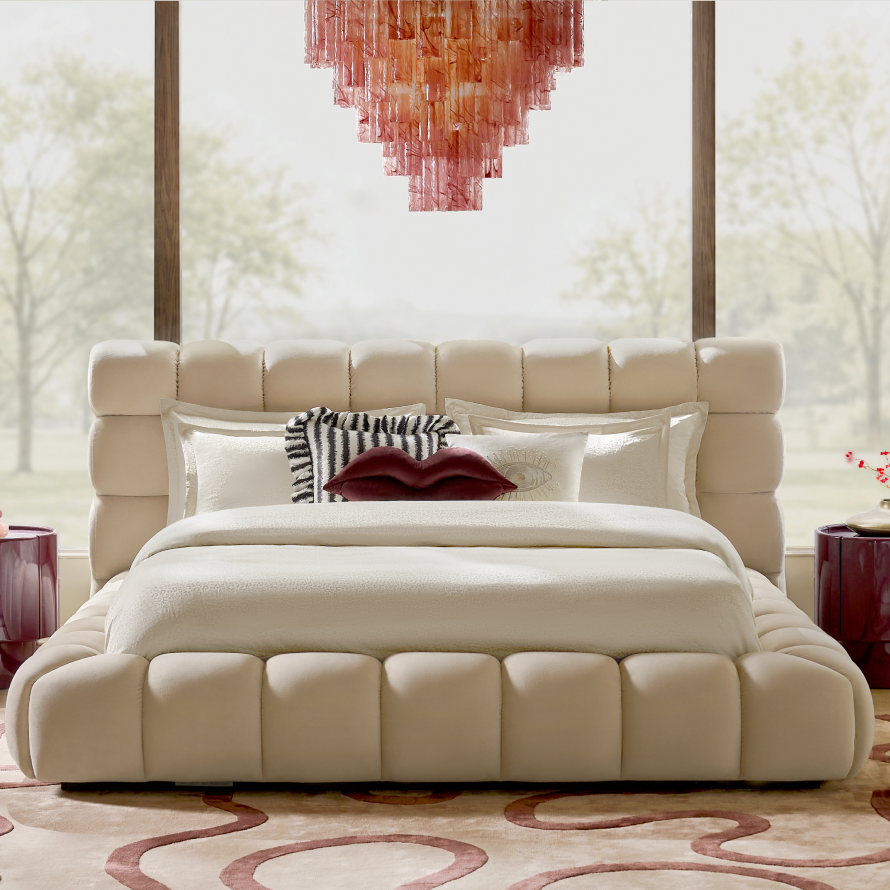 Modern plush channeled cream upholstered platform bed styled with a red lip accent pillow beneath a pink glass chandelier.