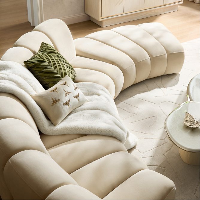Top-down view of a modern cream curved channel-tufted sectional sofa layered with a plush throw and accent pillows.