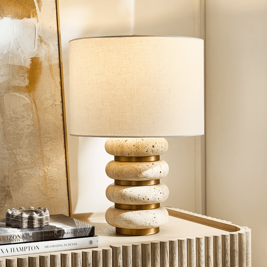 Modern table lamp with stacked travertine stone rings and brass accents on a fluted wood nightstand
