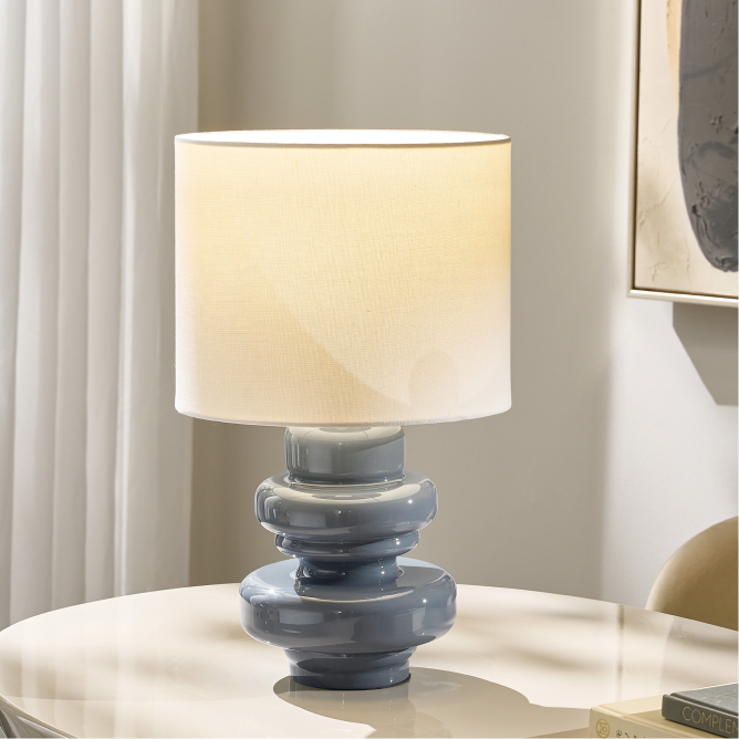 Modern table lamp featuring a glossy slate blue stacked geometric ceramic base and a white fabric drum shade.