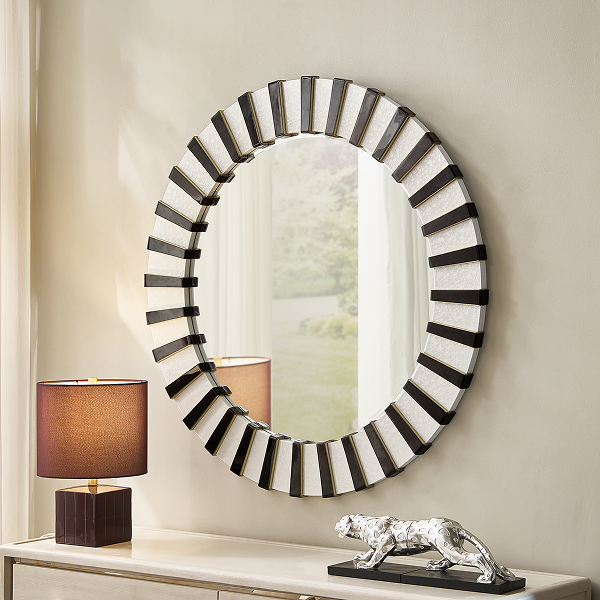 Large round wall mirror with a black and white striped sunburst frame, mounted above a console table with a small table lamp and jaguar figurine.