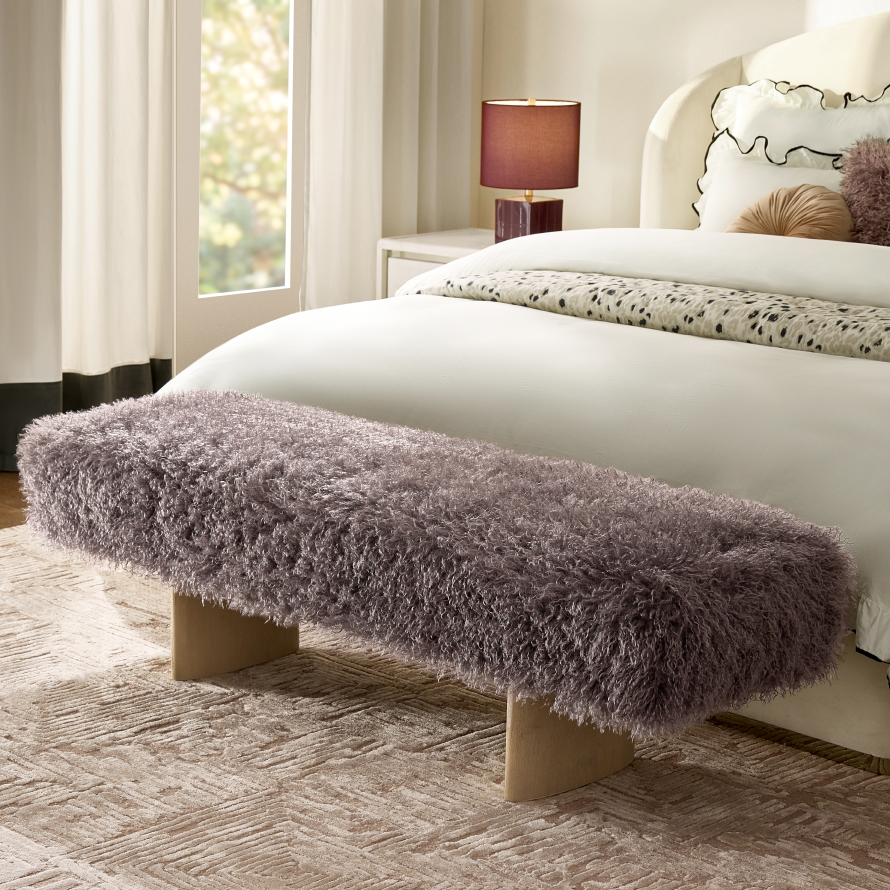 Modern plush shag upholstered bench with wooden pedestal legs placed at the foot of a white upholstered bed.