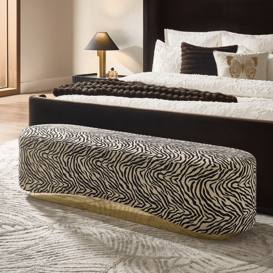 Oblong zebra print upholstered bedroom bench with brass base styled in front of a dark modern platform bed.