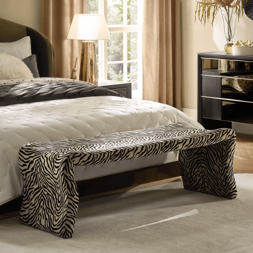 Zebra print upholstered waterfall bench positioned at the foot of a bed with layered white bedding.