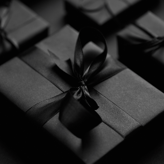 Black gift boxes wrapped with elegant black satin bows arranged closely together. title: Refer friends and family to Z Gallerie to give and get 5 percent rewards
