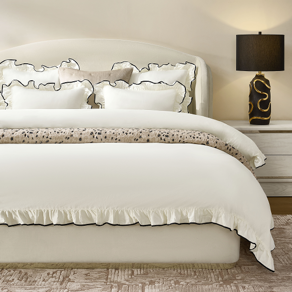 White luxury duvet cover and sham set with delicate ruffle trim, dressed on a modern upholstered bed.