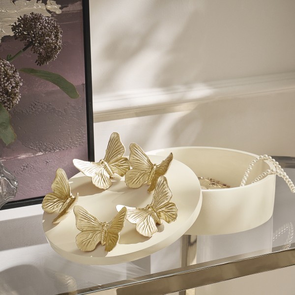 Decorative cream jewelry box adorned with sculpted gold butterflies on the lid, displayed on a glass tabletop.