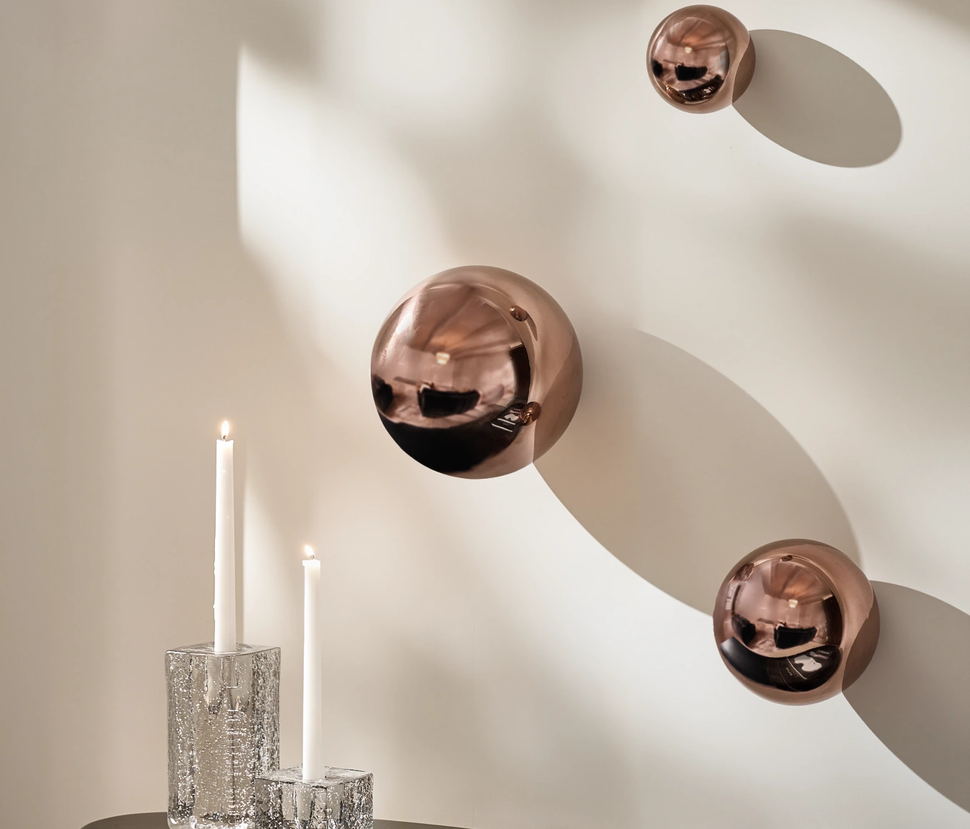 Trio of glossy bronze sphere wall art sculptures casting shadows above crystal taper candleholders.