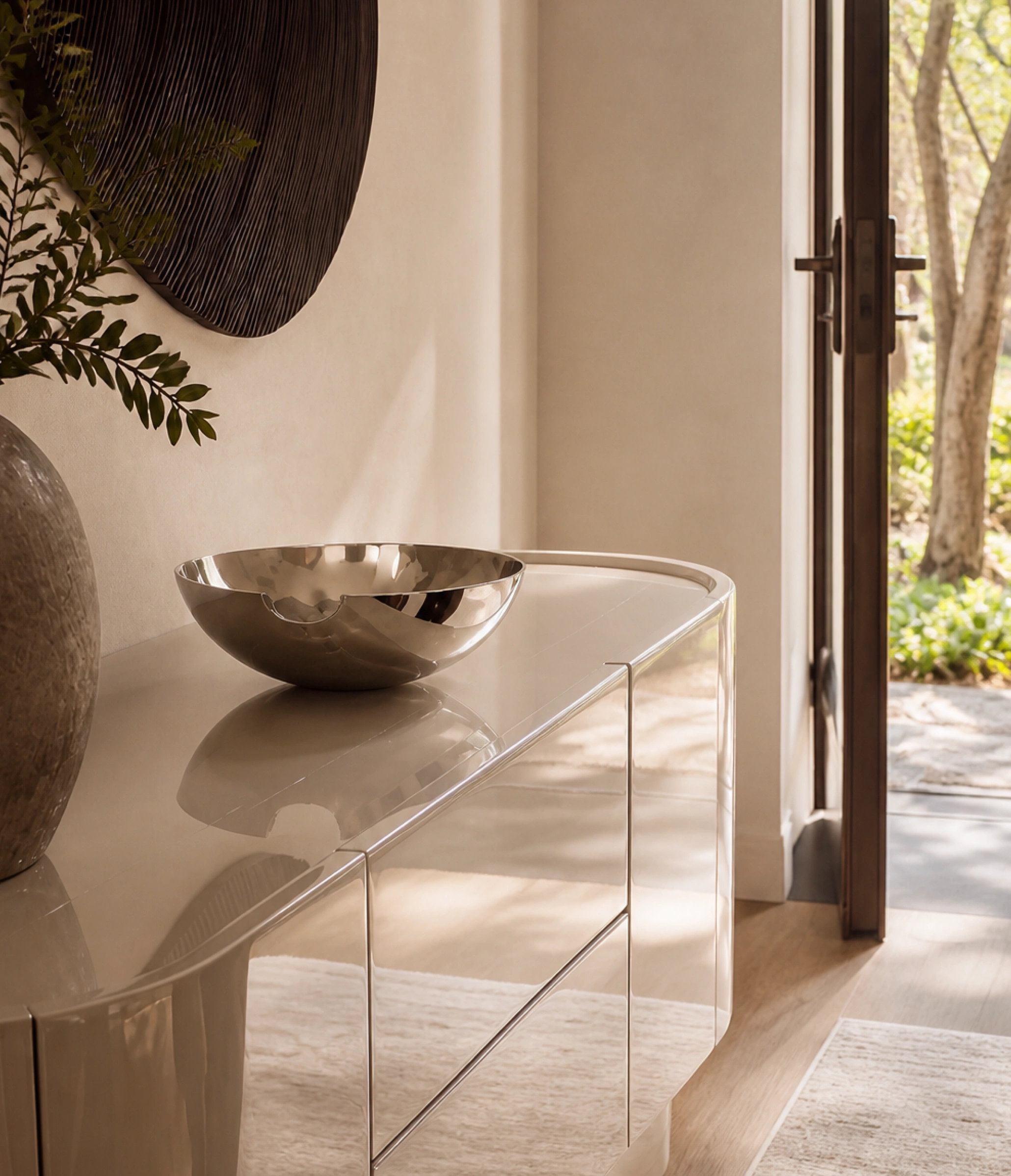 High-gloss lacquered entryway credenza with chrome trim styled with a polished silver decorative bowl and organic textured vase.