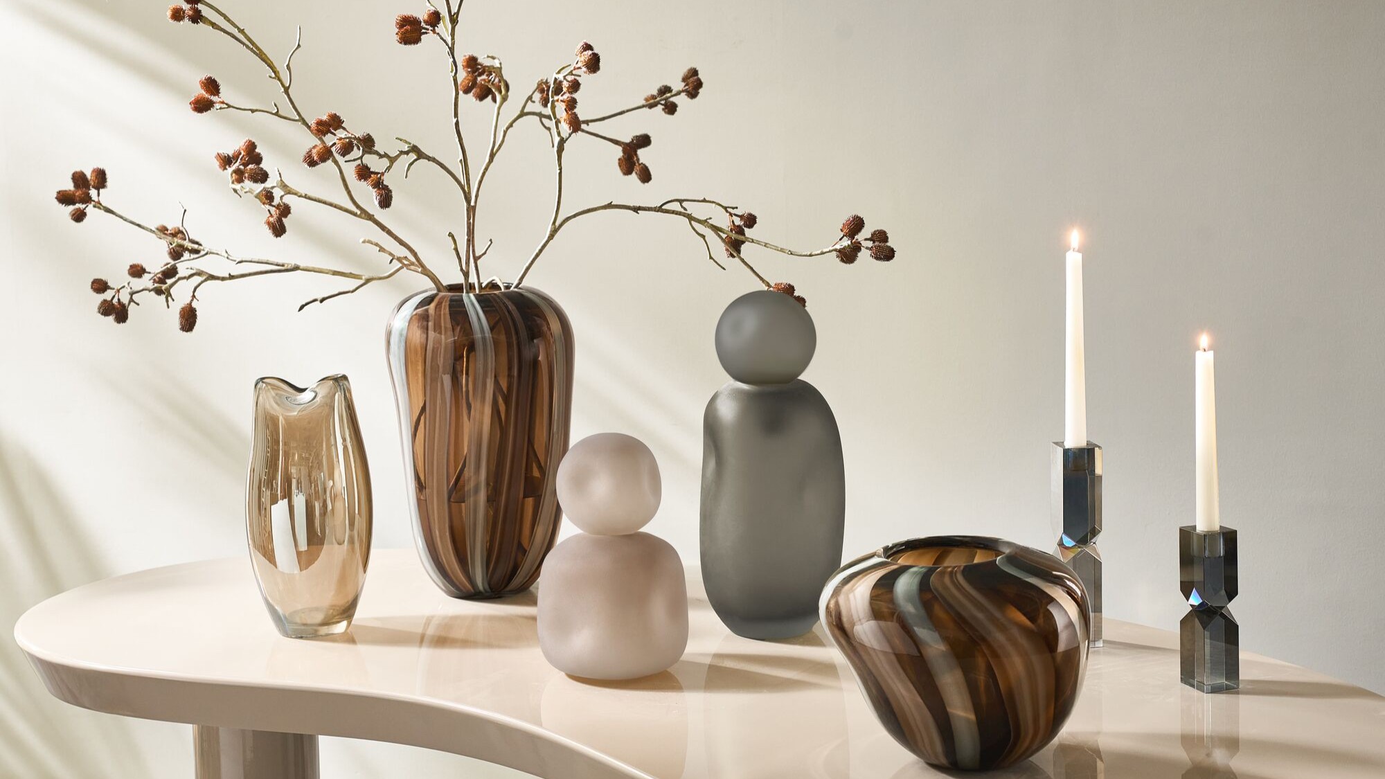 Smoky glass and softened forms create a tabletop moment that feels collected, calm, and considered.