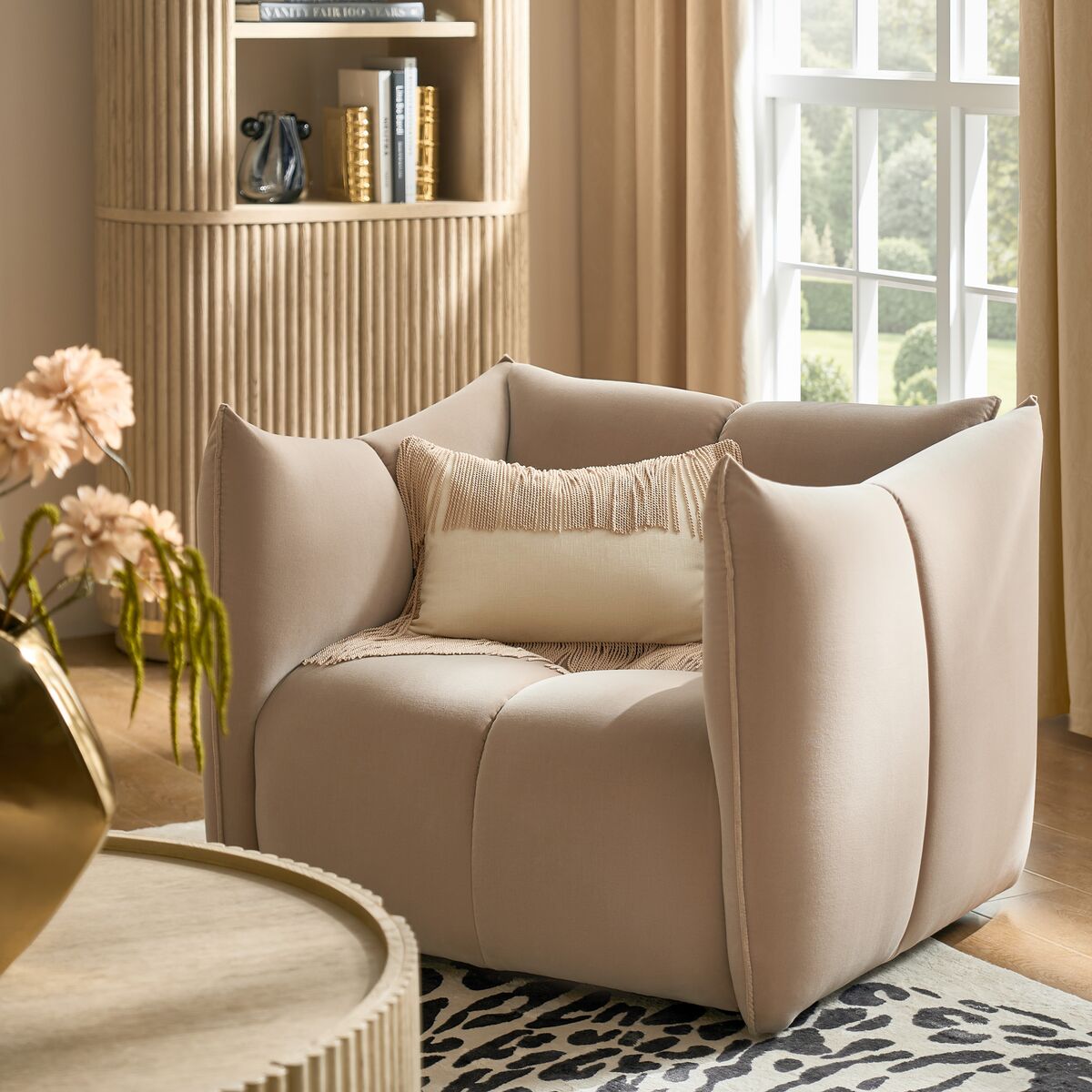 Modern beige sculptural accent armchair paired with a lumbar pillow on a zebra pattern rug next to fluted cabinetry.