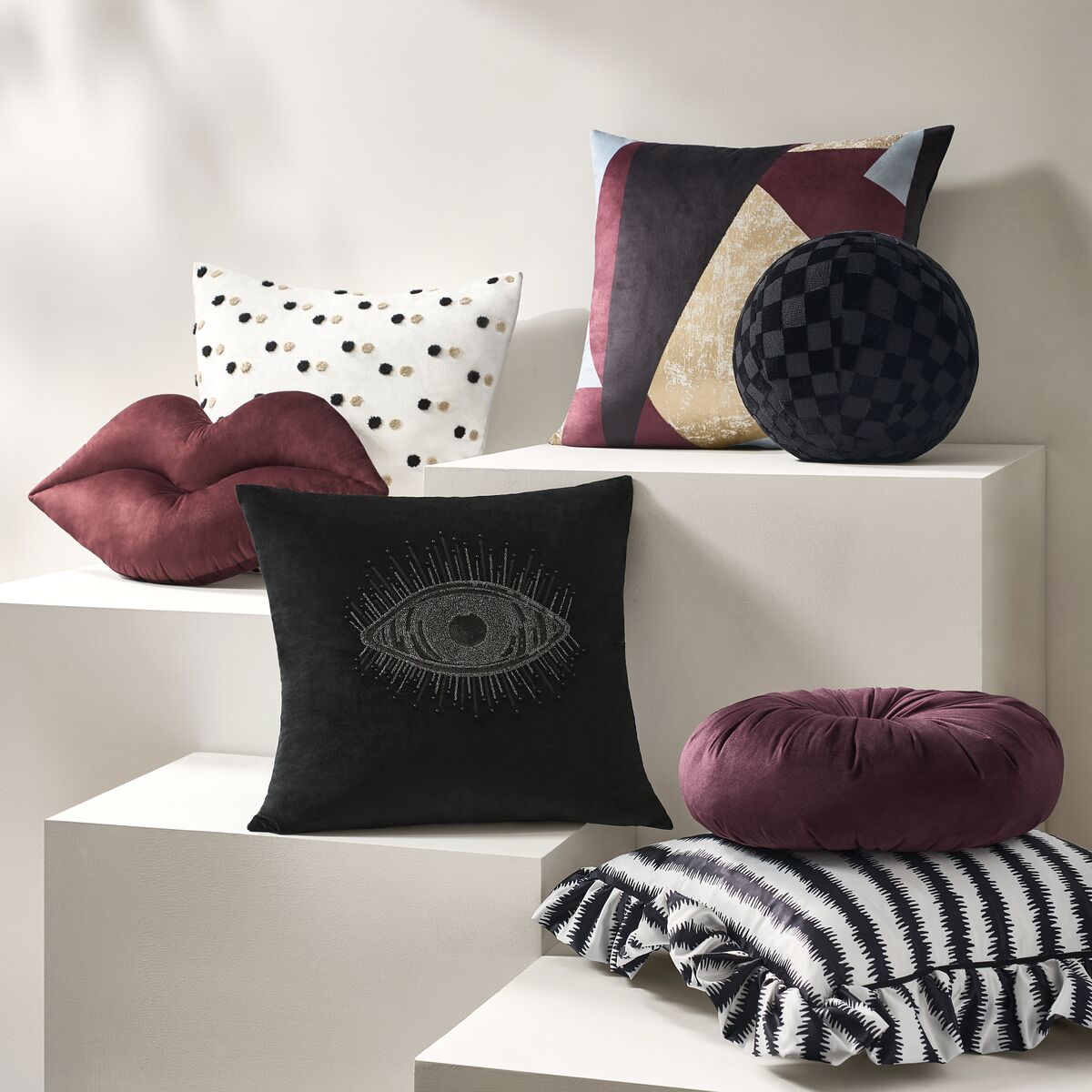 Gallery arrangement of luxury decorative throw pillows featuring lip-shaped cushion, embroidered black pillow, colorblock velvet, and round pleated accents.