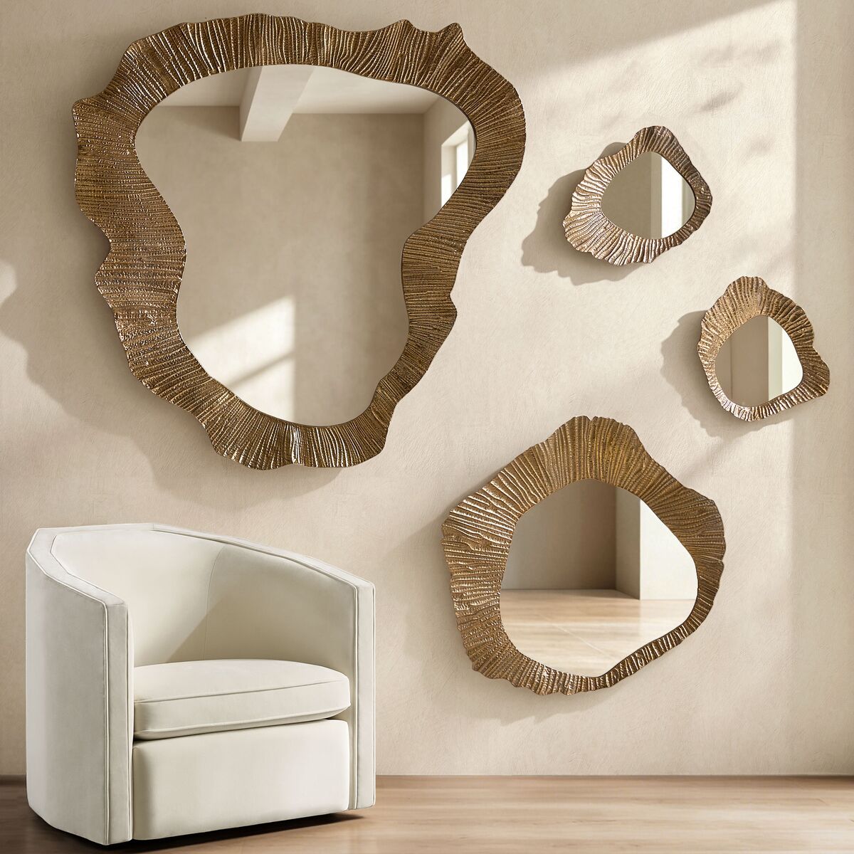 Set of asymmetrical organic-shaped wall mirrors with textured gold frames displayed above a white barrel armchair.