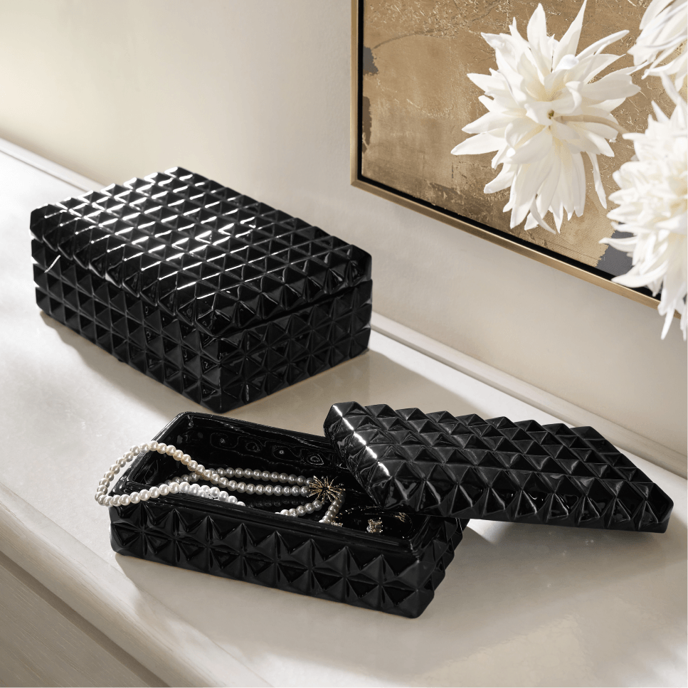 Pair of black studded glass jewelry boxes displayed on a white surface with pearl jewelry.