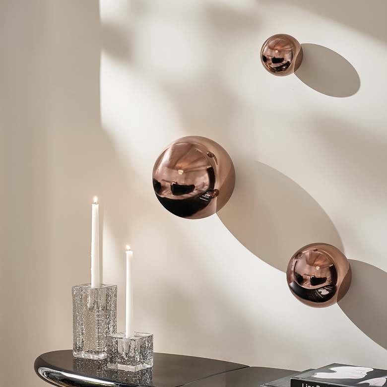 Metallic rose gold spherical wall ornaments paired with clear glass taper candle holders.