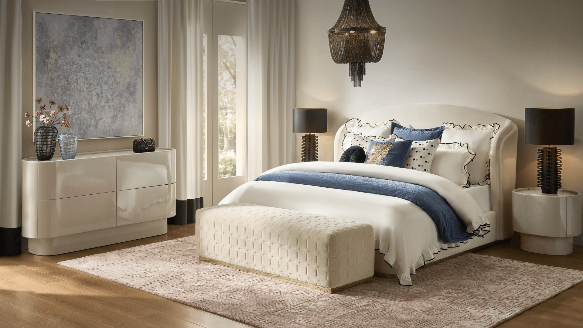 Elegant modern bedroom suite featuring a curved wingback upholstered bed, cream woven bed bench, glossy white curved dresser, and black beaded chandelier.