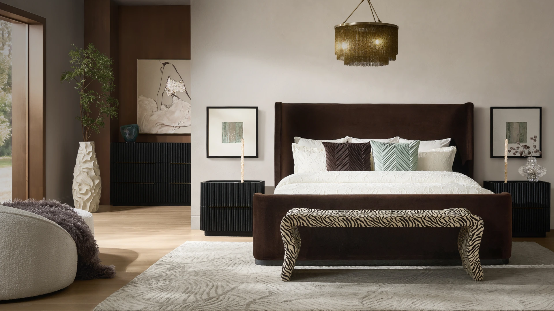 Luxurious bedroom featuring a dark brown tufted upholstered platform bed with crisp white bedding, accent pillows, matching nightstands with table lamps, and a warm amber glass chandelier.