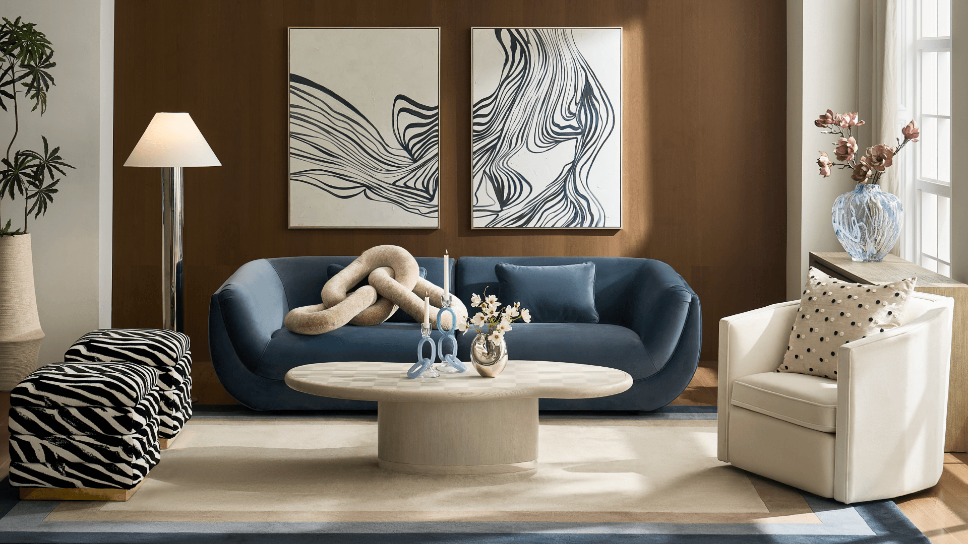 Modern living room featuring a curved blue velvet sofa, oval pedestal coffee table, zebra-print accent ottomans, cream swivel armchair, and abstract black-and-white canvas art.