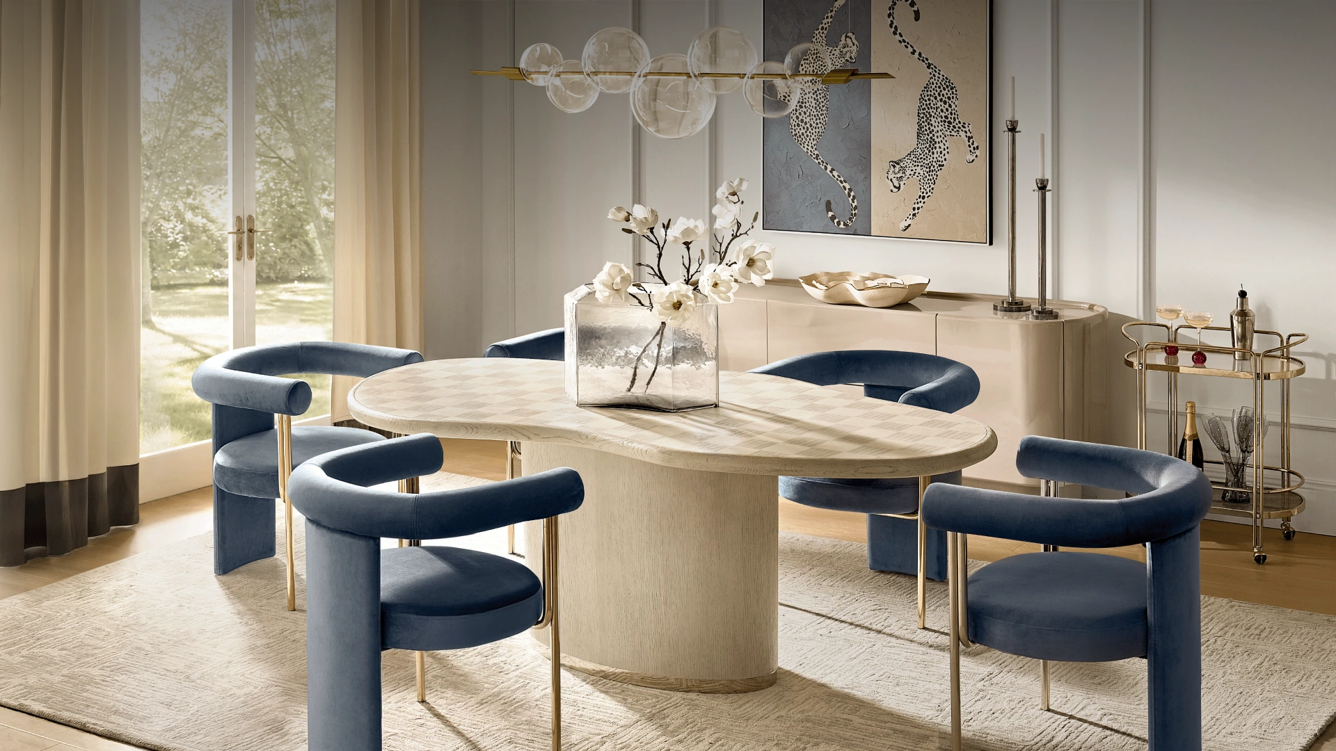 Modern dining room setup with an organic shaped wood dining table, curved navy blue velvet dining chairs, and a gold bar cart.