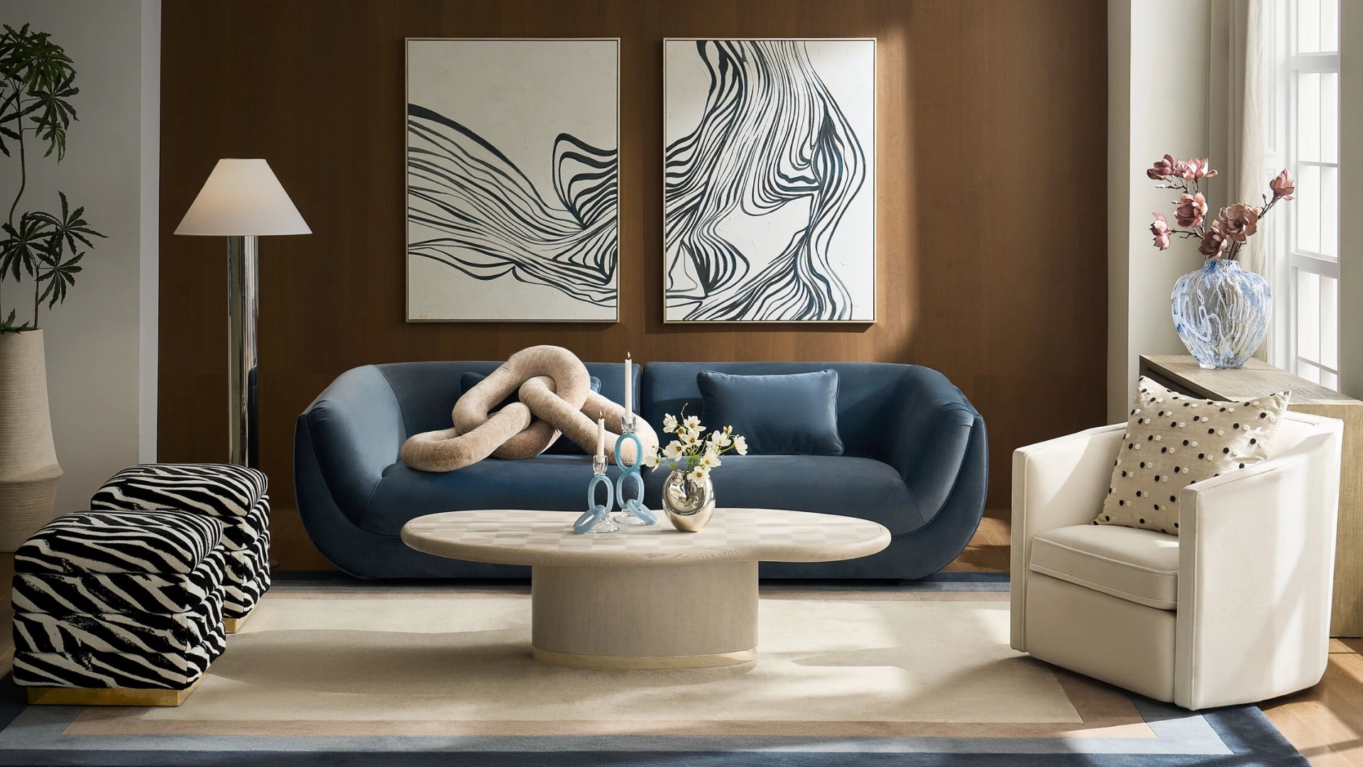 Modern living room featuring a curved blue velvet sofa, oval pedestal coffee table, zebra-print accent ottomans, cream swivel armchair, and abstract black-and-white canvas art.