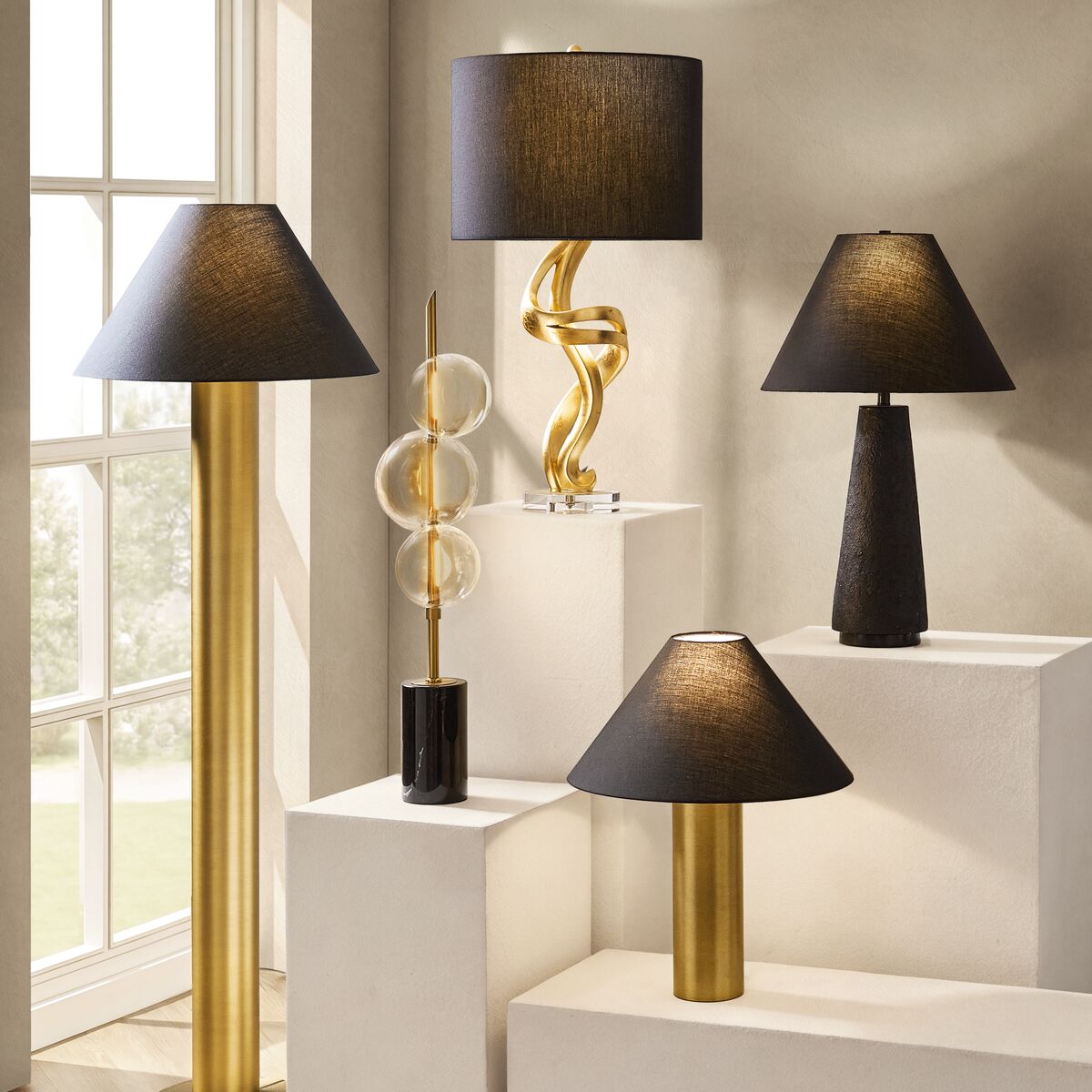 Collection of modern table and floor lamps featuring black shades and sculpted gold, brass, and dark ceramic bases.