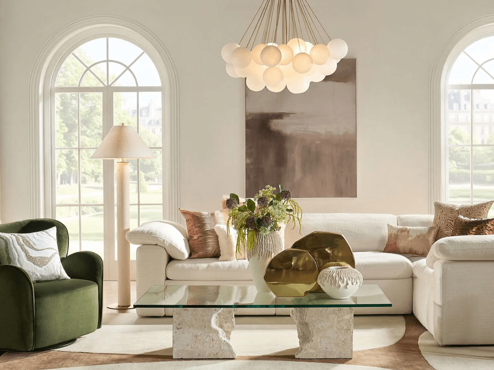 Elegant living room featuring a glass coffee table, cream modular sofa, green swivel chair, and an illuminated cloud frosted glass chandelier.