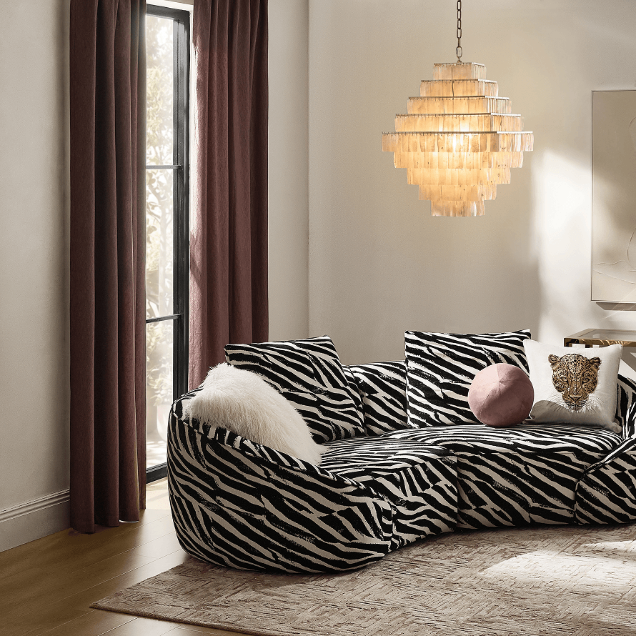 Modern curved sectional sofa in bold black and white zebra print styled with throw pillows beneath a tiered crystal chandelier.