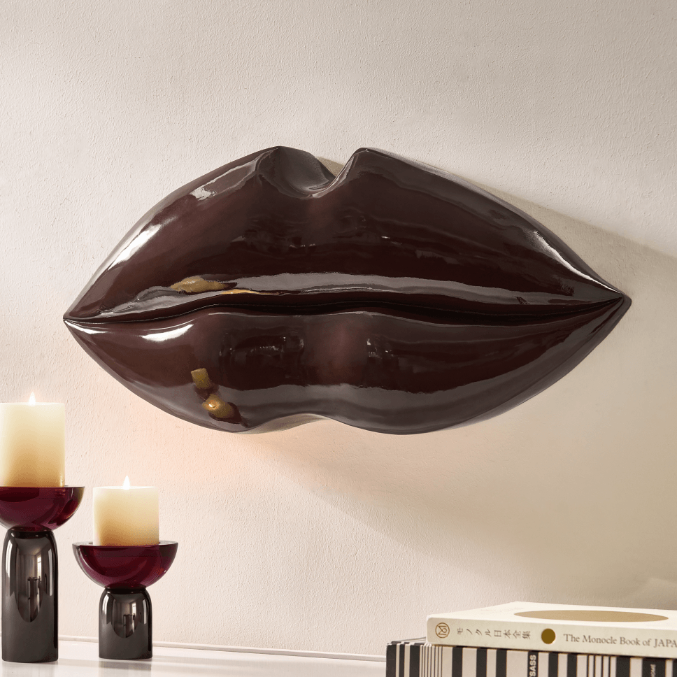 Sculptural high-gloss burgundy lips wall art mounted above small pillar candleholders.