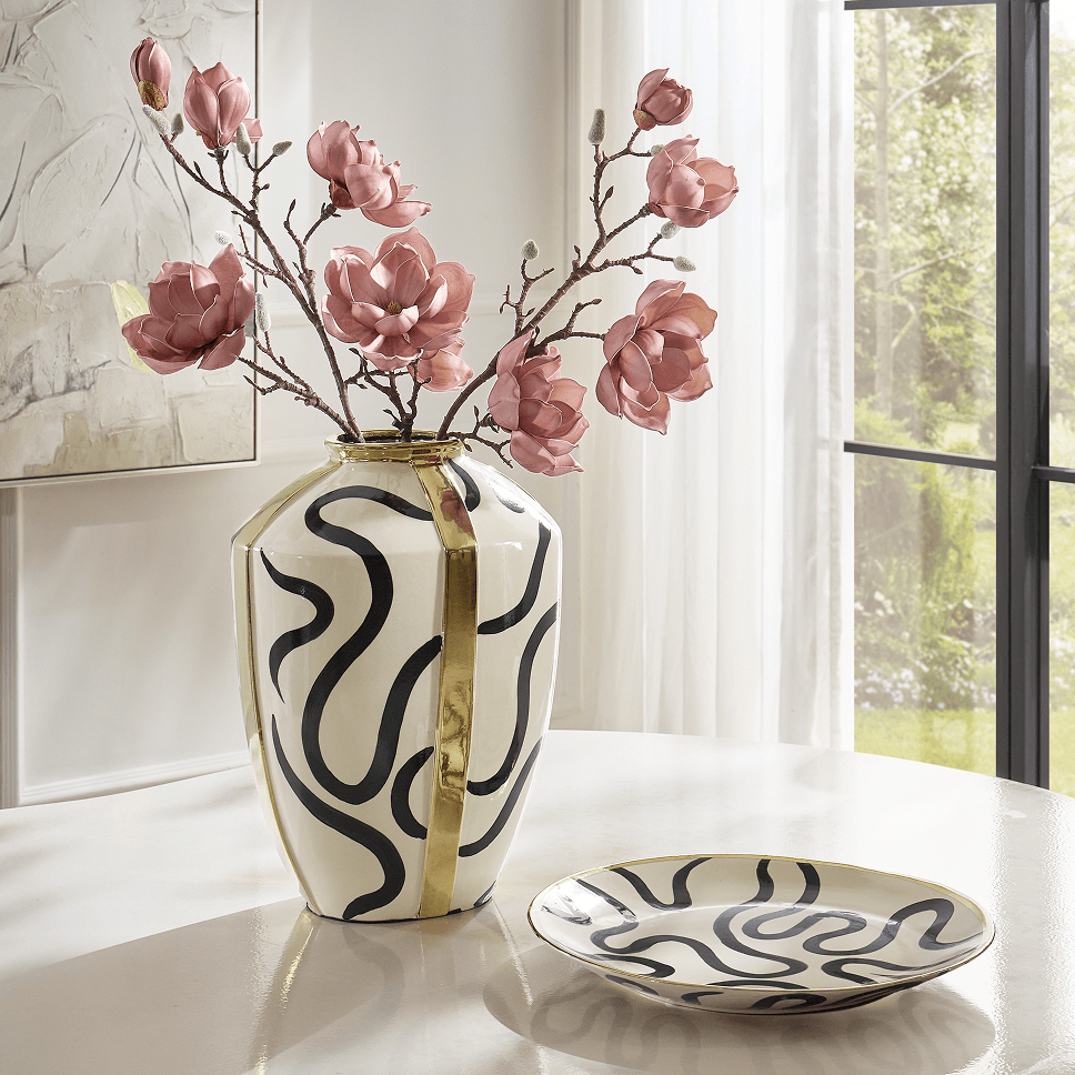 Ceramic vase with black squiggle patterns and gold metallic trim filled with pink blossoms, paired with a matching decorative catchall dish.