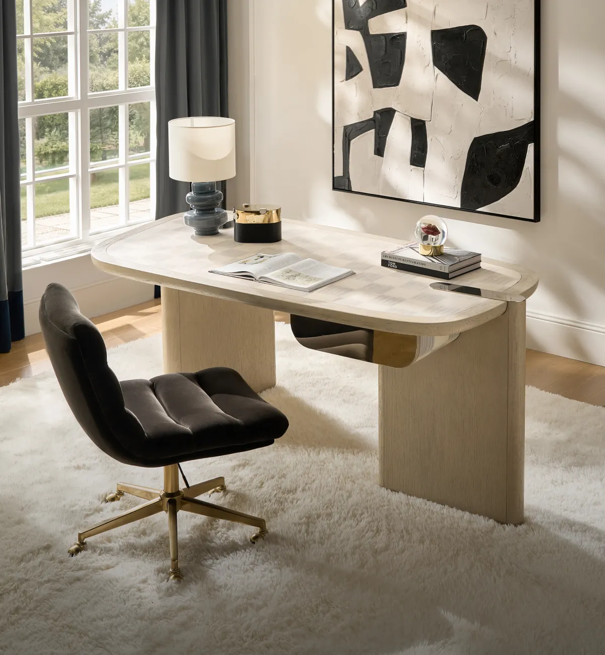 A modern luxury home office with a curved light oak executive desk, a charcoal black velvet swivel chair, a slate blue lamp, and black-and-white abstract wall art.