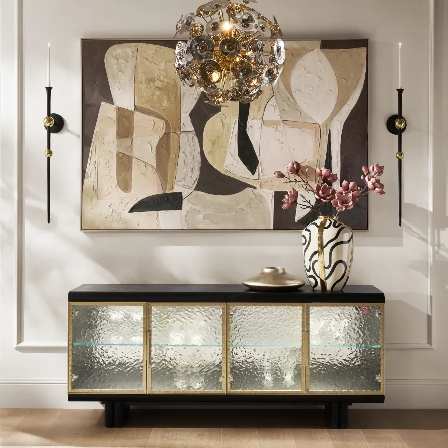 Elegant foyer scene featuring a black wooden credenza with hammered glass doors, a large abstract textured painting, a brass glass disc chandelier, and a black-and-white patterned vase.