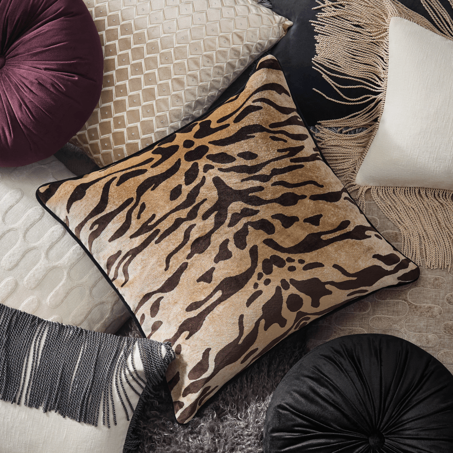 Layered collection of luxury throw pillows showcasing a bold tiger print cushion, deep plum velvet round pillow, and textured neutral geometric pillows.