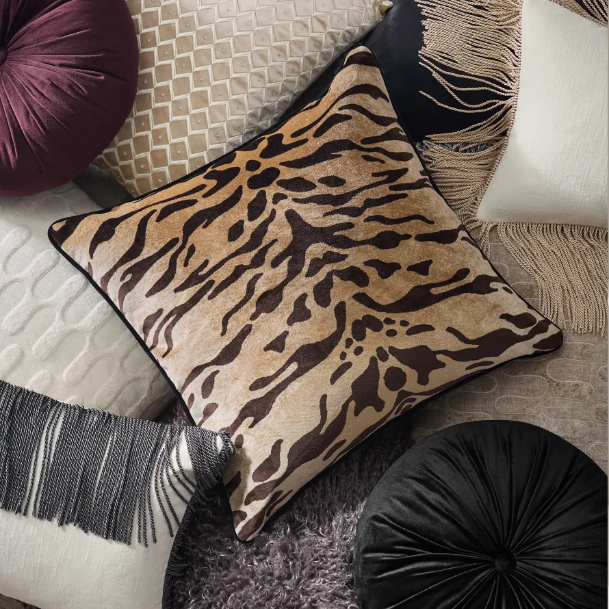 A rich assortment of luxury throw pillows featuring a center tiger-print pillow, round velvet cushions, geometric beaded pillows, and fringe trim accents.