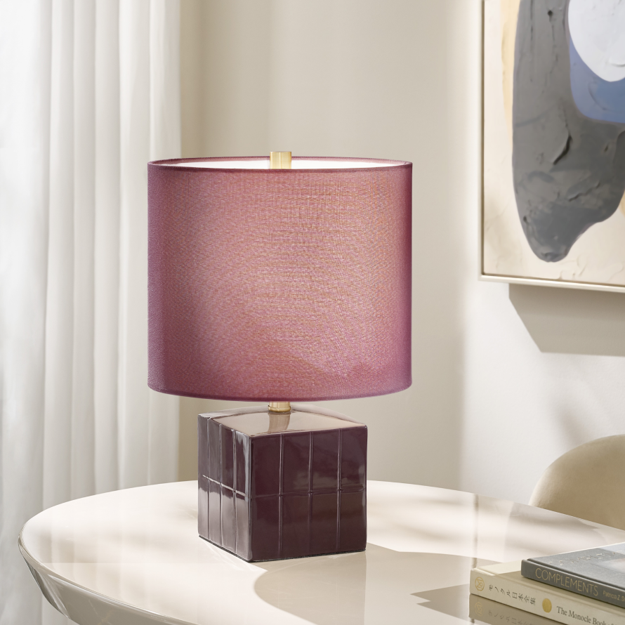 Modern designer table lamp with a plum shade and high-gloss tiled base set on a lacquered tabletop.