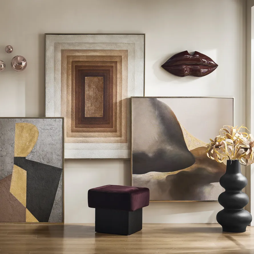 A gallery-style arrangement featuring earth-toned abstract canvases, a glossy burgundy lip wall sculpture, a dark velvet stool, and a matte black totem vase.