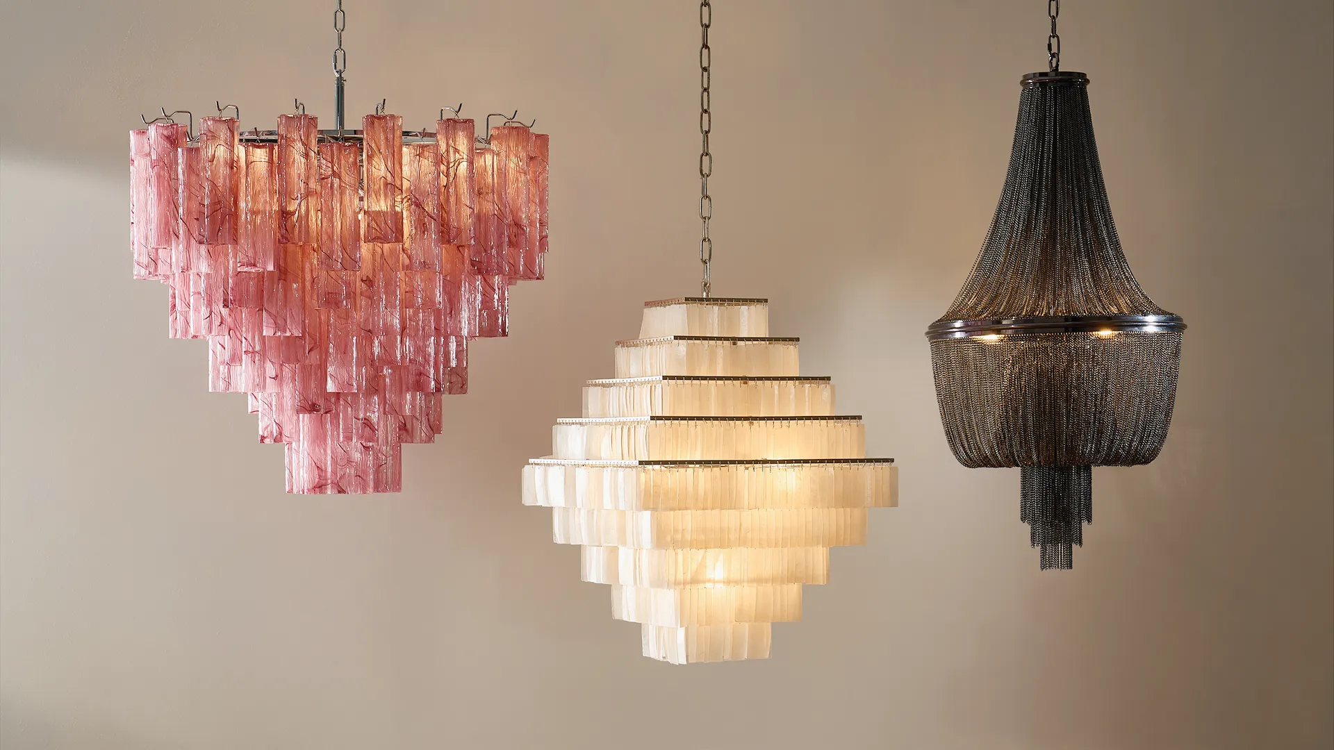 Three luxury statement chandeliers: a pink textured glass tiered chandelier, a mother-of-pearl shell diamond chandelier, and a dark metal chain empire chandelier.